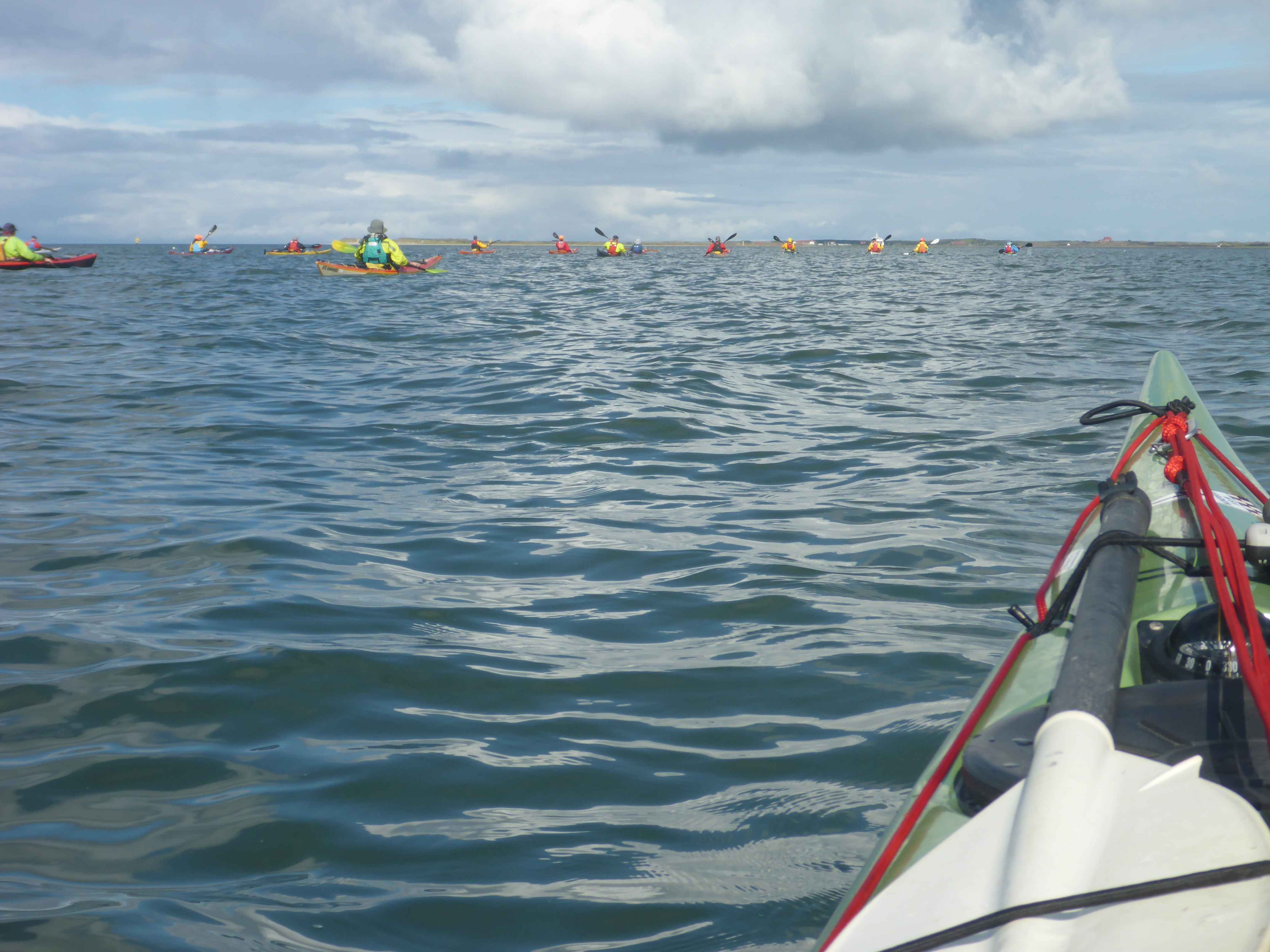 Eine Gruppe von Seekajakfahrenden auf dem Wasser. Im Hintergrund die Insel Spiekeroog